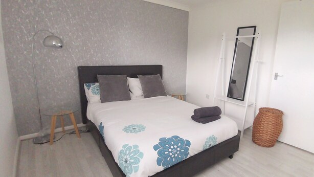 A bedroom with a bed, a bedside table, a lamp, a mirror, and a door.