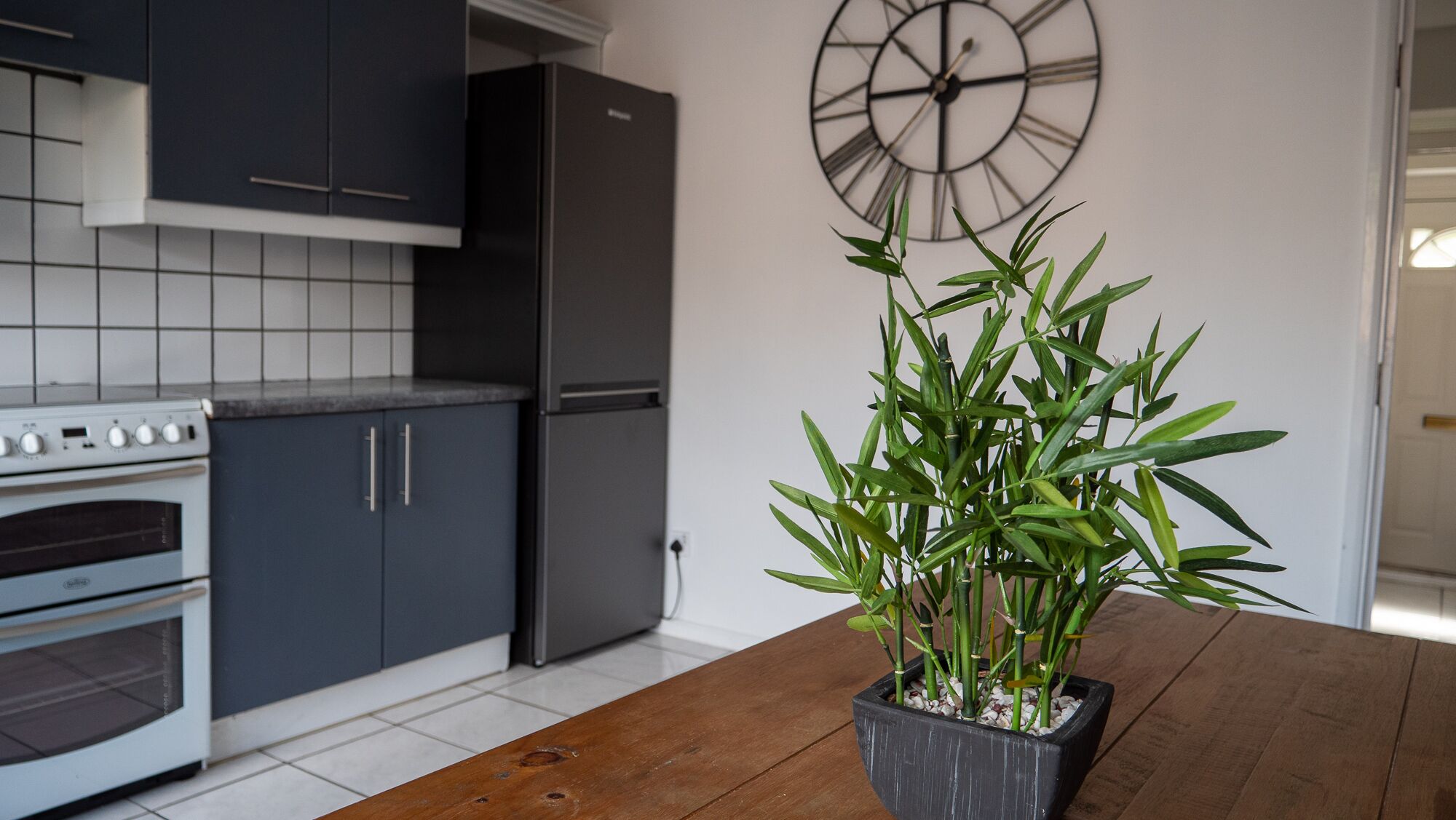 A kitchen with dark cabinets, a white oven, and a large clock on the wall.