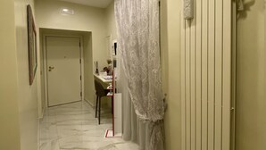A hallway with a marble floor, a radiator, a desk with a chair, and a door at the end. - Porto Rooms & Suite (Naples)