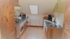 A compact kitchen with wooden cabinets, a microwave, a kettle, and a sink.