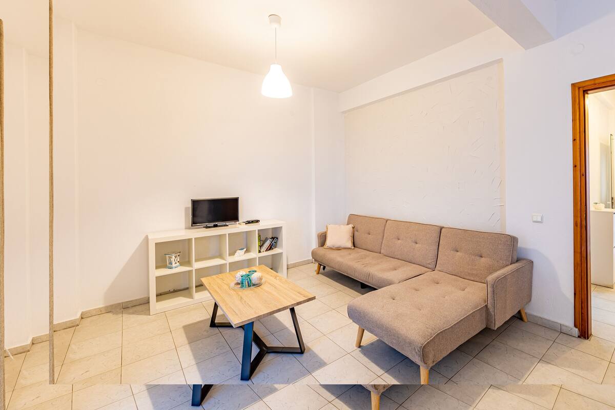 A modern living room with a sectional sofa, a wooden coffee table, a TV on a white shelf, and a pendant light.
