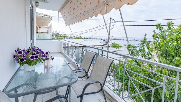 A balcony with a glass table, chairs, and a potted plant with purple flowers. - Skioni Apartments (Kassandra)