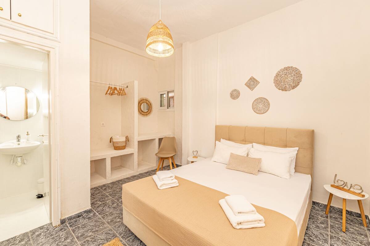 A hotel room with a large bed, a bedside table, a mirror, a hanging light fixture, and a small round table with a decorative item.