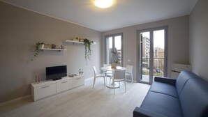 Uma sala de estar moderna com televisão de tela plana, móveis brancos, uma varanda com vista e uma luminária de teto.