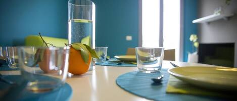 Una mesa de comedor con vasos transparentes, un vaso alto con una planta y un plato.