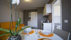 Uma cozinha moderna com armários brancos, um espaço de jantar com mesa posta para dois e uma planta sobre a mesa.