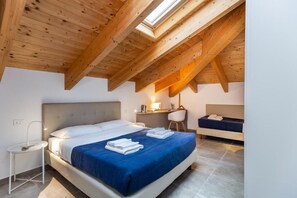 A bedroom with a bed, bedside table, desk, chair, and a small window.