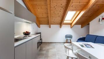 Una cuina moderna amb un fanal, una zona de menjador amb una taula i cadires blanques, i un sofà blau.