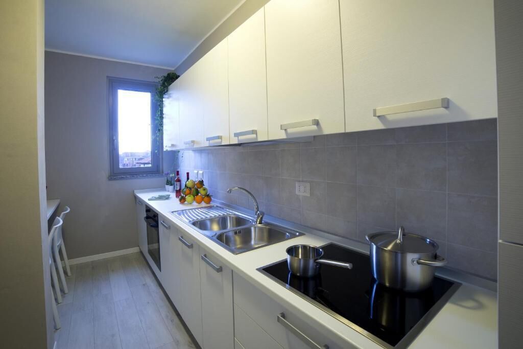A modern kitchen with white cabinets, a black stovetop, stainless steel sinks, and a window with a view.