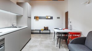 Uma cozinha moderna com forno embutido, uma área de refeições com mesa e cadeiras brancas, e um banco com uma bolsa.