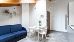 Um interior moderno com um sofá azul, uma mesa de jantar branca com cadeiras e uma área de cozinha.