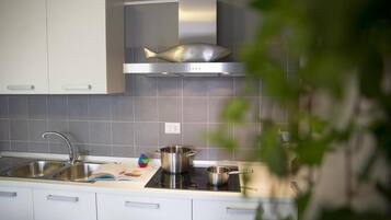 Et moderne køkken med hvide skabe, en emhætte i fiskedesign i rustfrit stål og en gasblus.