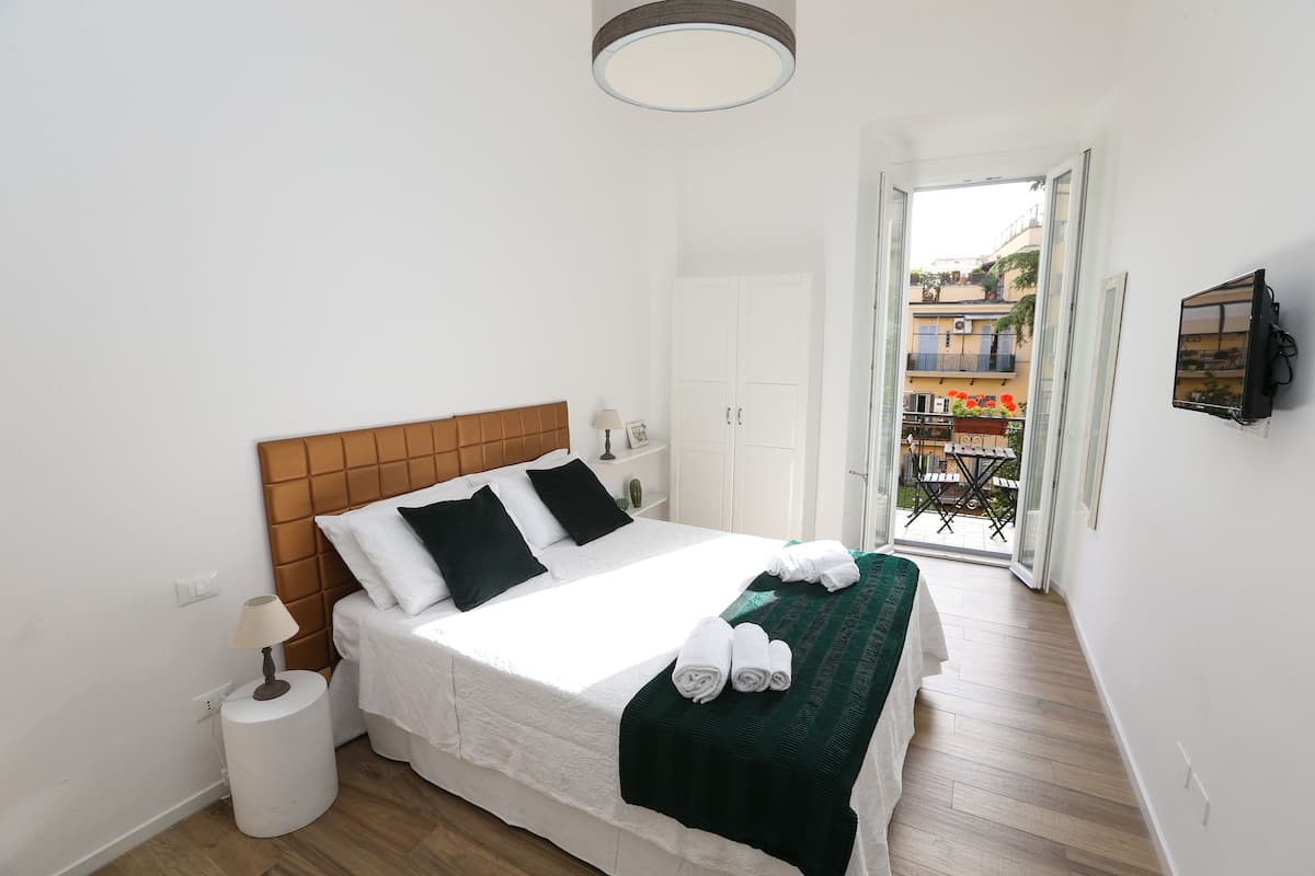 Un lit bien fait, avec une tête de lit en bois, une lampe de chevet et un plaid vert.