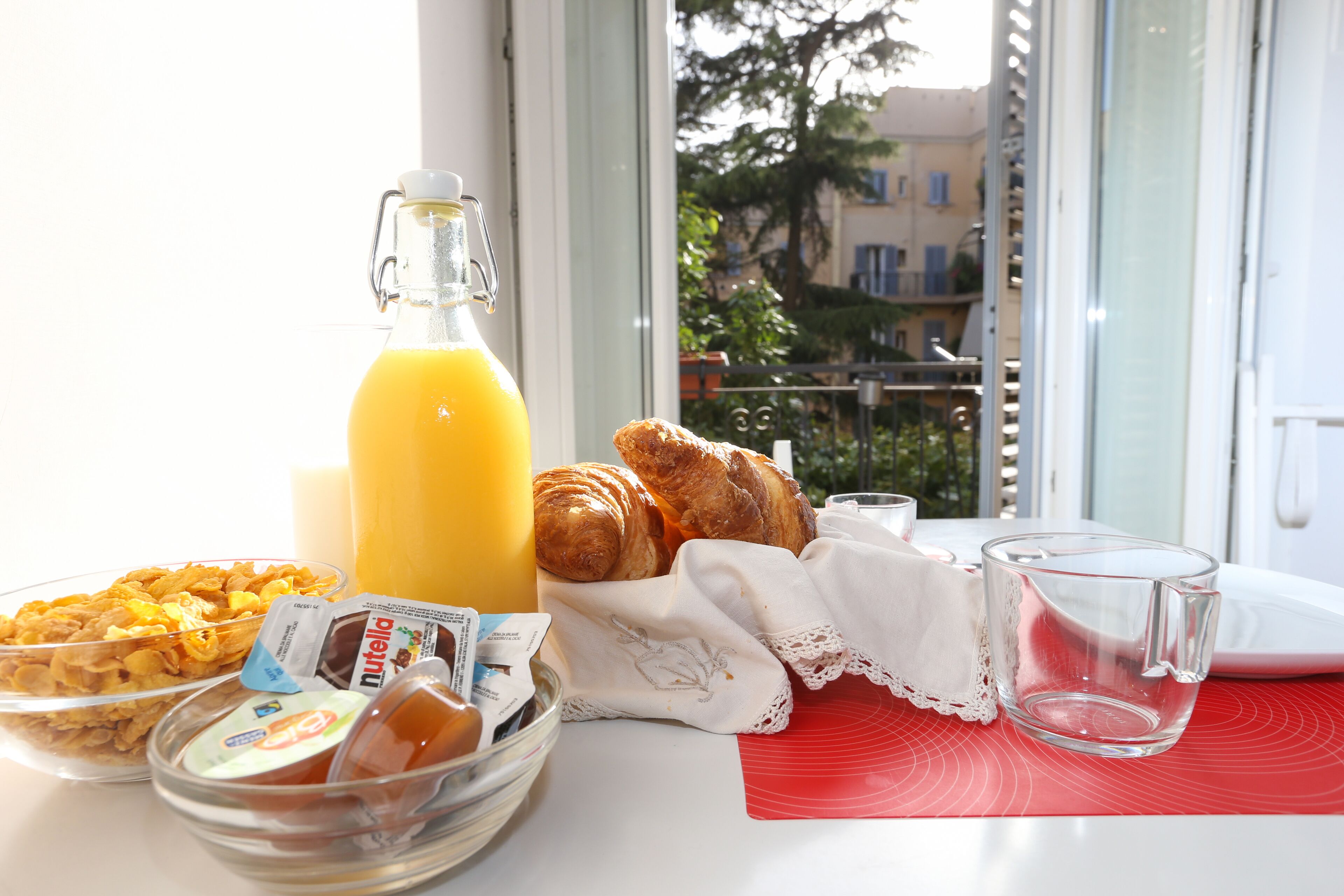 Una tavola imbandita per la colazione con croissant, cereali, succo di frutta e un bicchiere d'acqua.