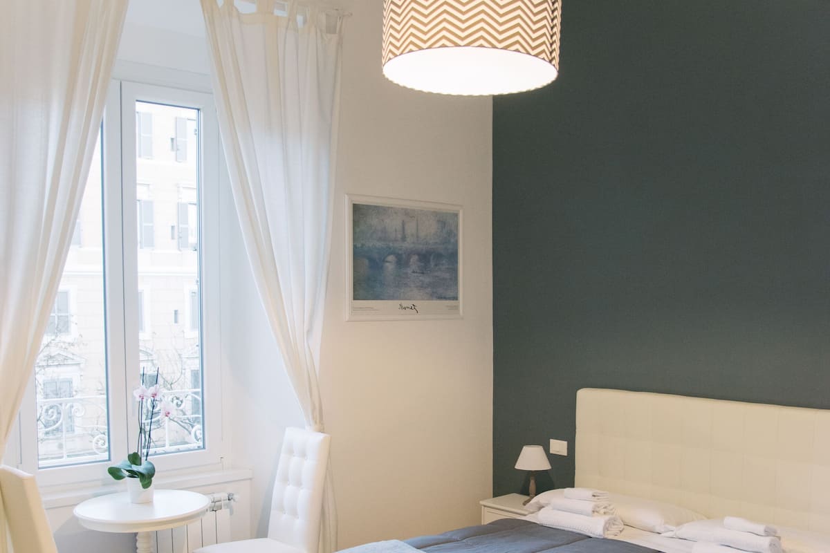 Une chambre à coucher avec un lit, une chaise, une table et une fenêtre avec des rideaux.