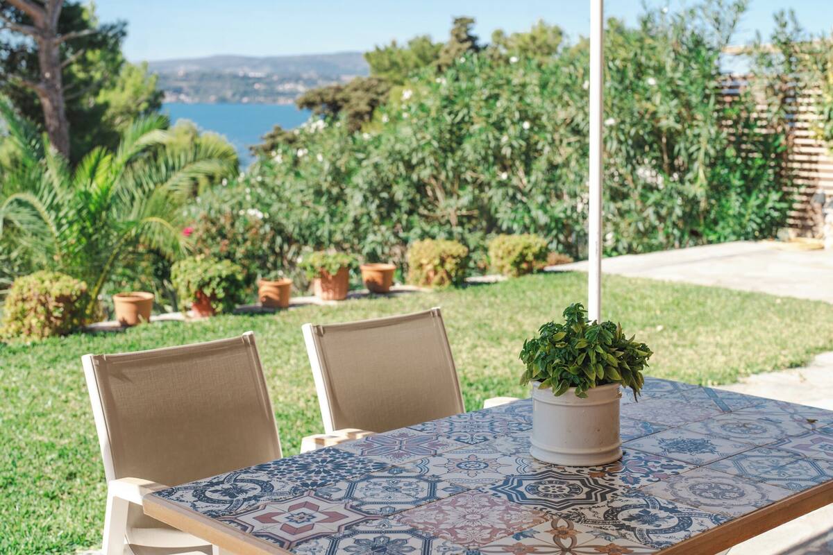 An outdoor patio with a patterned table, two chairs, and a potted plant.