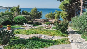 A landscaped garden with a stone pathway leading to a seating area, overlooking a body of water. - Anthoula's House (Kefalonia)