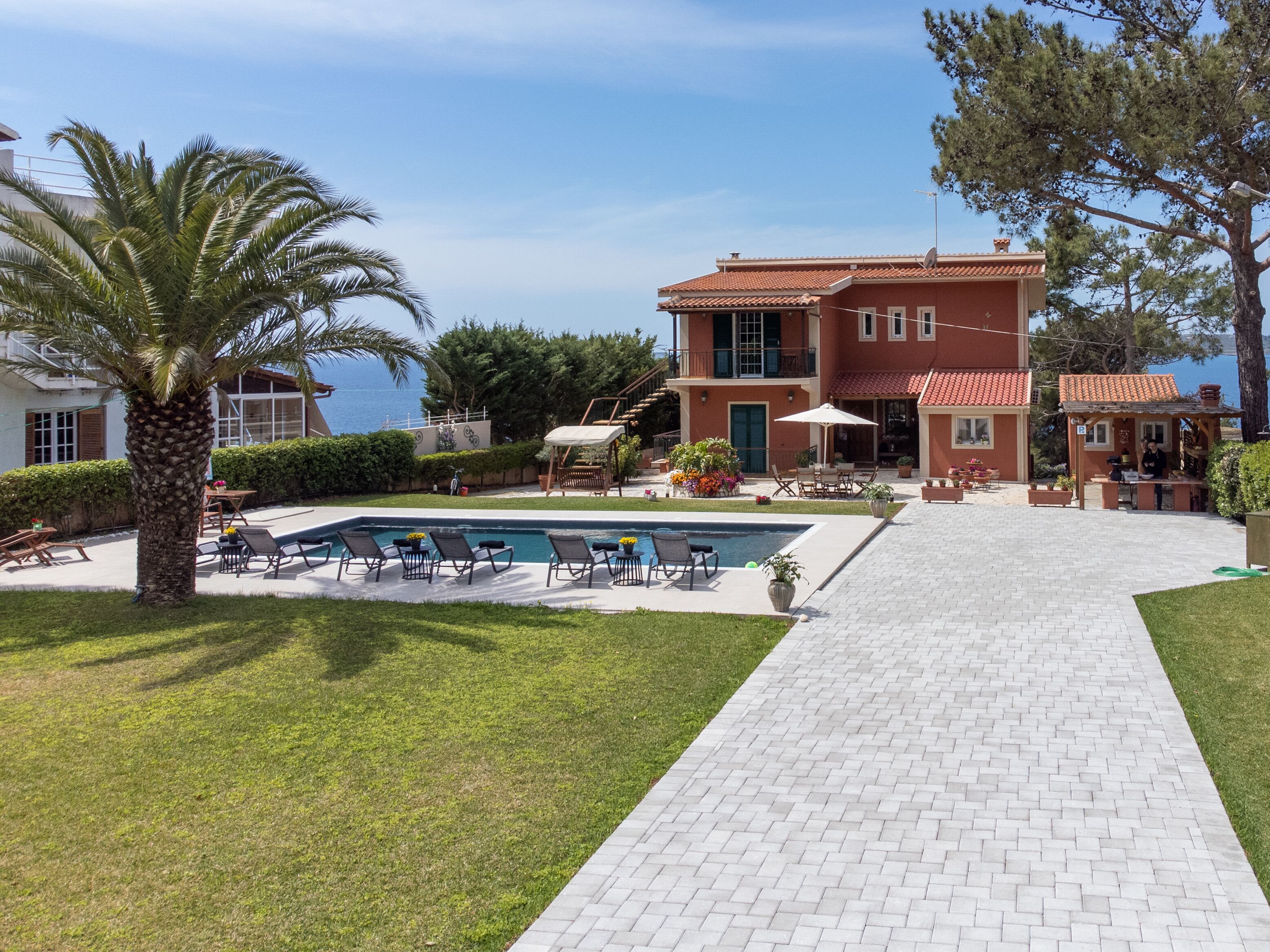 Un edificio de dos pisos con piscina, asientos al aire libre y vista al mar.
