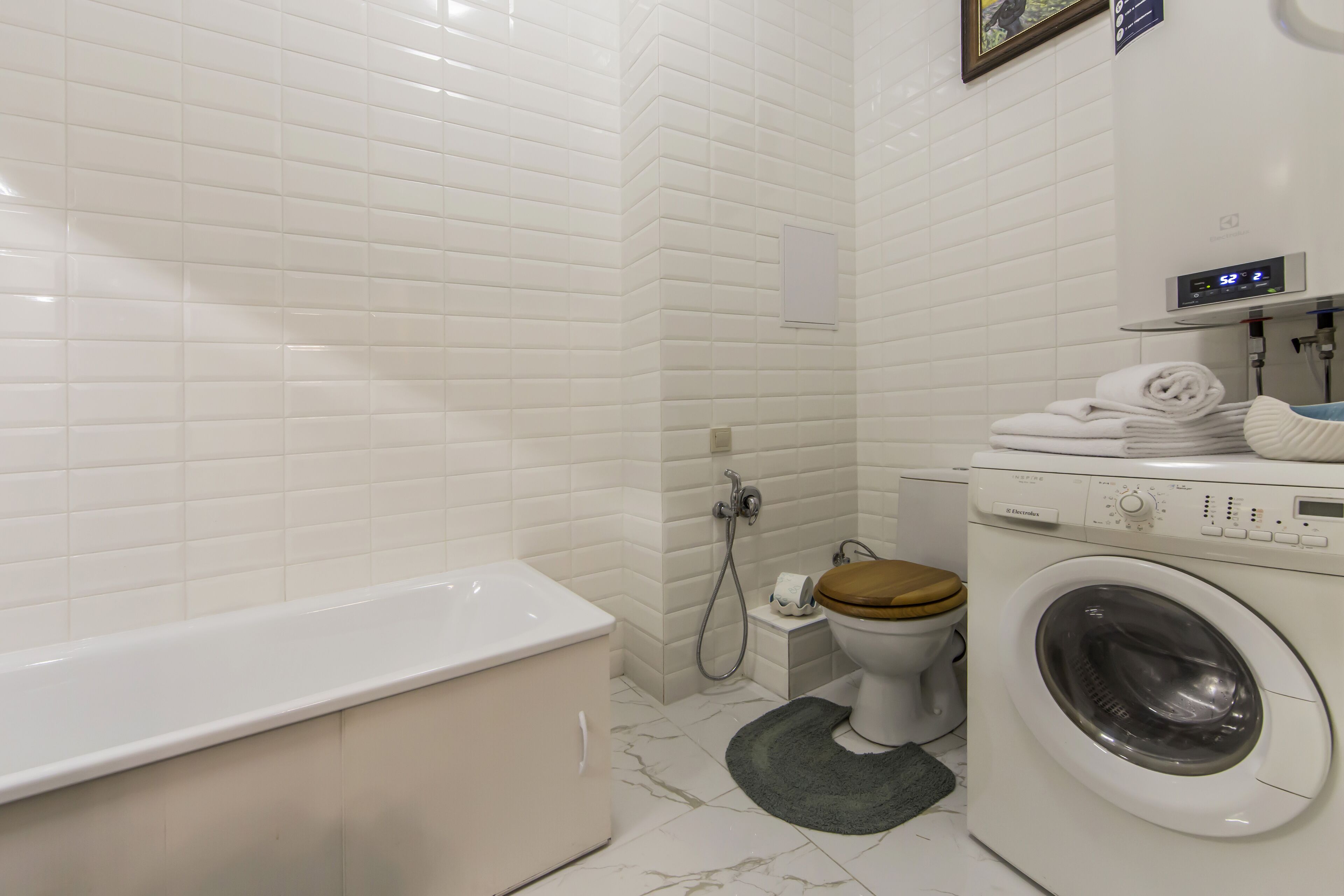 Et moderne badeværelse med en hvid flisevæg, et hvitt badekar, en vaskemaskine og et toilet.