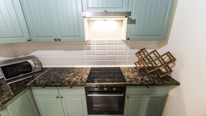 Una cucina con mobili color petrolio, un piano cottura nero, un forno a microonde e una dispensa in legno.