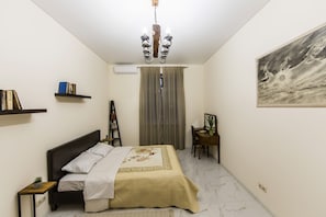 Une chambre à coucher comprenant un lit, un bureau, une chaise, une bibliothèque, un lustre et un tableau accroché au mur.
