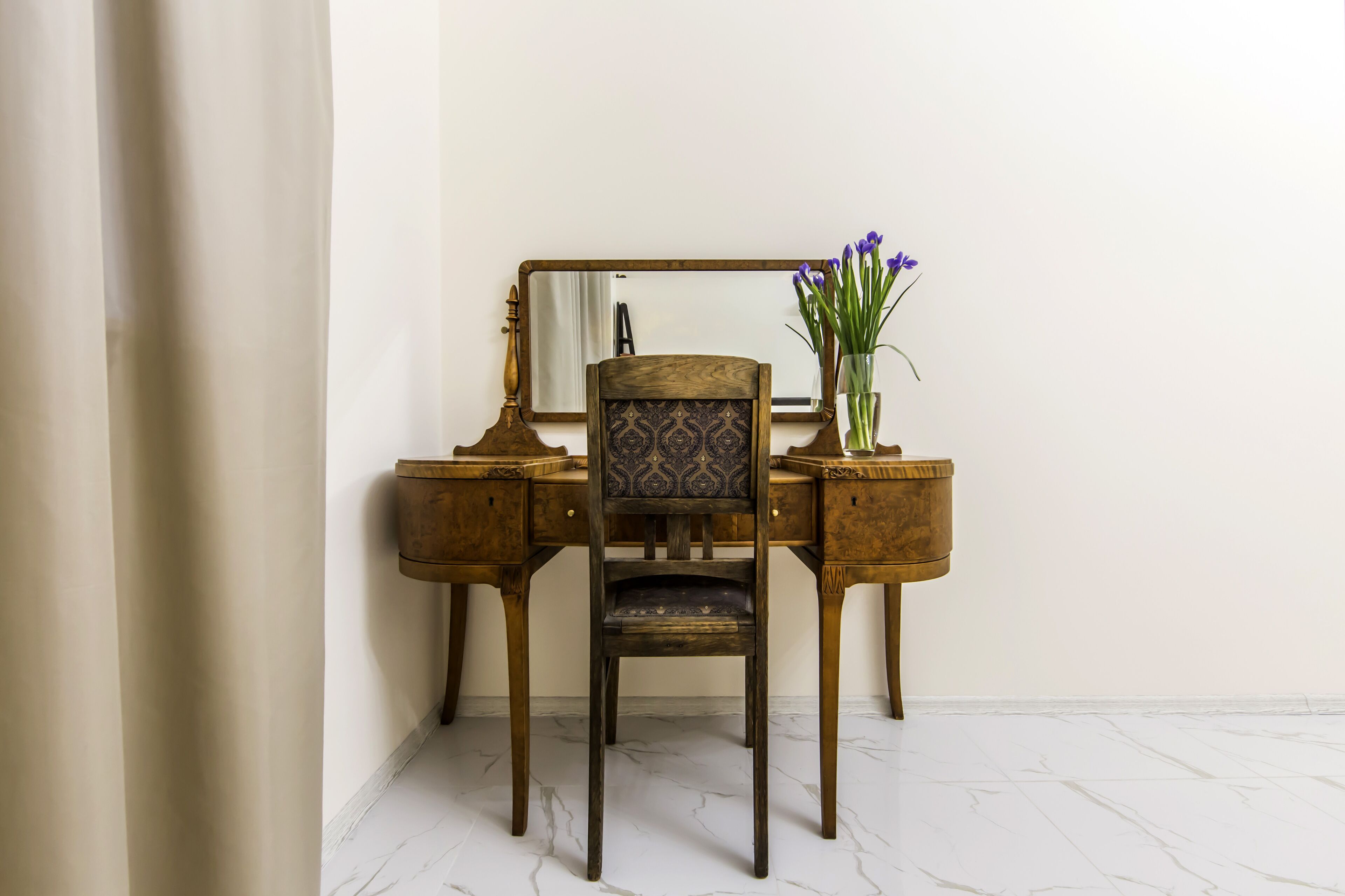 Un bureau en bois, avec un miroir et un vase de fleurs.