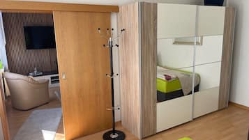 Ein Zimmer mit einem Bett, einem Kleiderständer, einem Fernseher und einer Holztür.