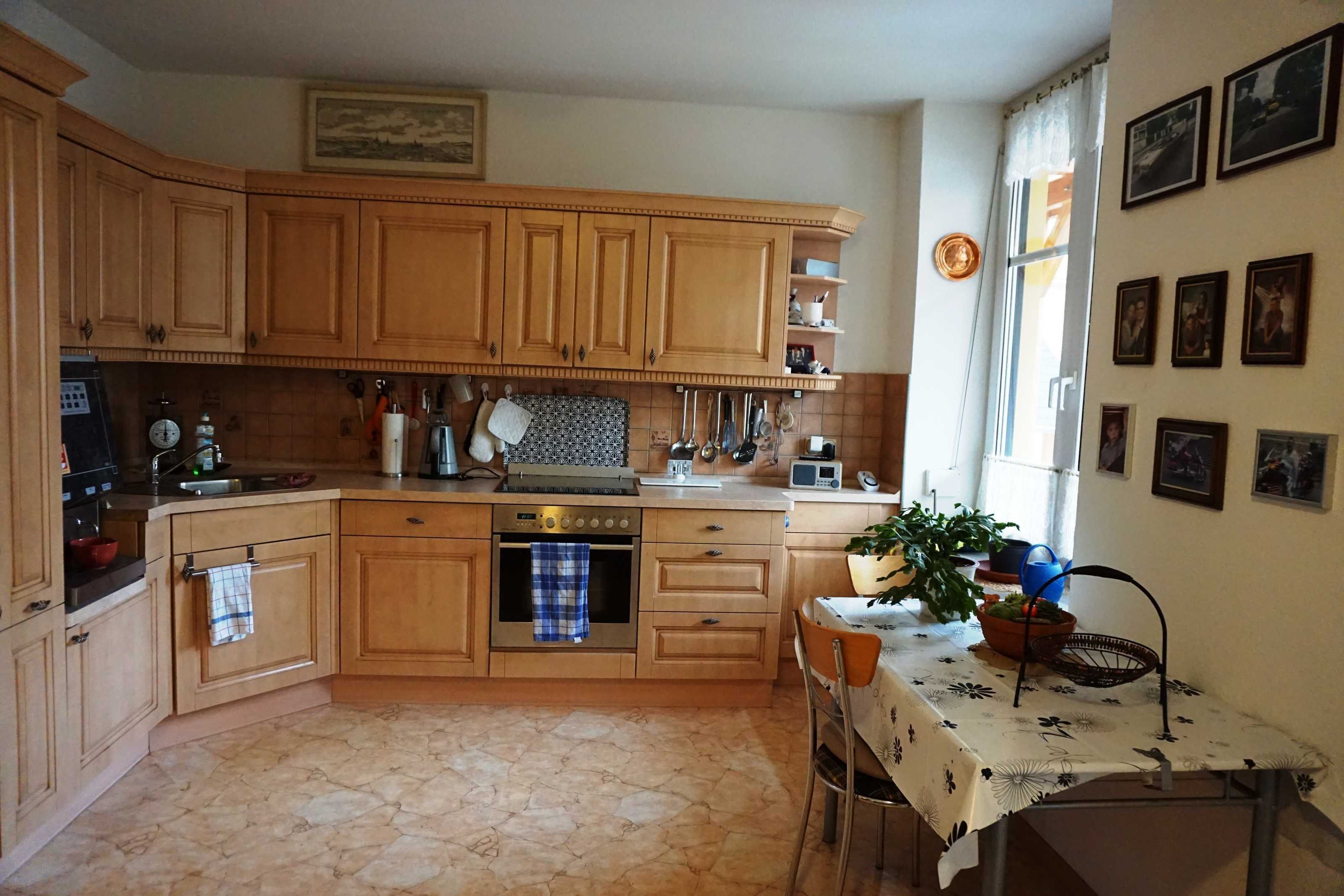 Une cuisine avec des meubles de rangement en bois, une cuisinière, un évier et une table à manger recouverte d’une nappe.