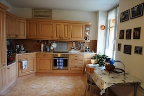 A kitchen with wooden cabinets, a stove, a sink, and a dining table with a tablecloth. - Holiday apartment - private room at the Ginkgo tree (Erfurt)