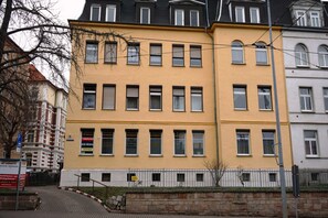 A multi-story building with a yellow facade, multiple windows, and a brick base.