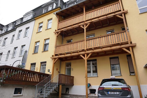 A multi-story building with balconies, a staircase, and a parked car.