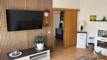Ein modernes Wohnzimmer mit Flachbildfernseher, Holzpaneele, einem kleinen Schrank, einer Lampe und einer Topfpflanze.