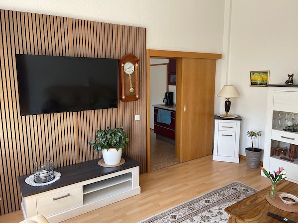 A modern living room with a flat-screen TV, wooden panel wall, a small cabinet, a lamp, and a potted plant. - Holiday apartment - private room at the Ginkgo tree (Erfurt)