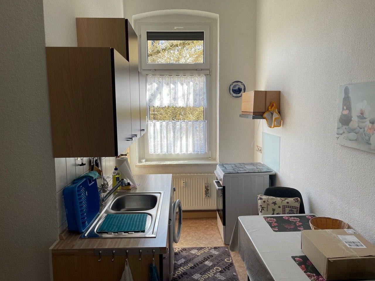 Une cuisine de taille réduite, dotée d’une fenêtre, d’un évier, d’une petite table et d’un radiateur.