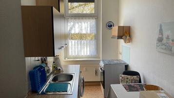 Une cuisine de taille réduite, dotée d’une fenêtre, d’un évier, d’une petite table et d’un radiateur.