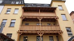 A multi-story building with a wooden balcony structure, multiple windows, and a visible door. - Holiday apartment - private room at the Ginkgo tree (Erfurt)
