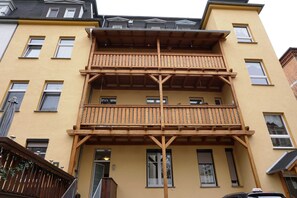 A multi-story building with a wooden balcony structure, multiple windows, and a visible door. - Holiday apartment - private room at the Ginkgo tree (Erfurt)