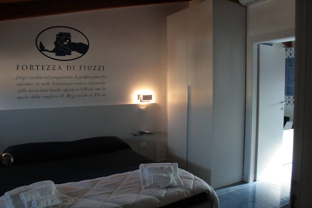 A hotel room with a bed, a wall-mounted sign, and a nightstand with a lamp.