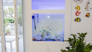 A white dining table with two potted plants, a fish tank, and a door leading to an outdoor area. - Praja Vecchia (Praia a Mare)