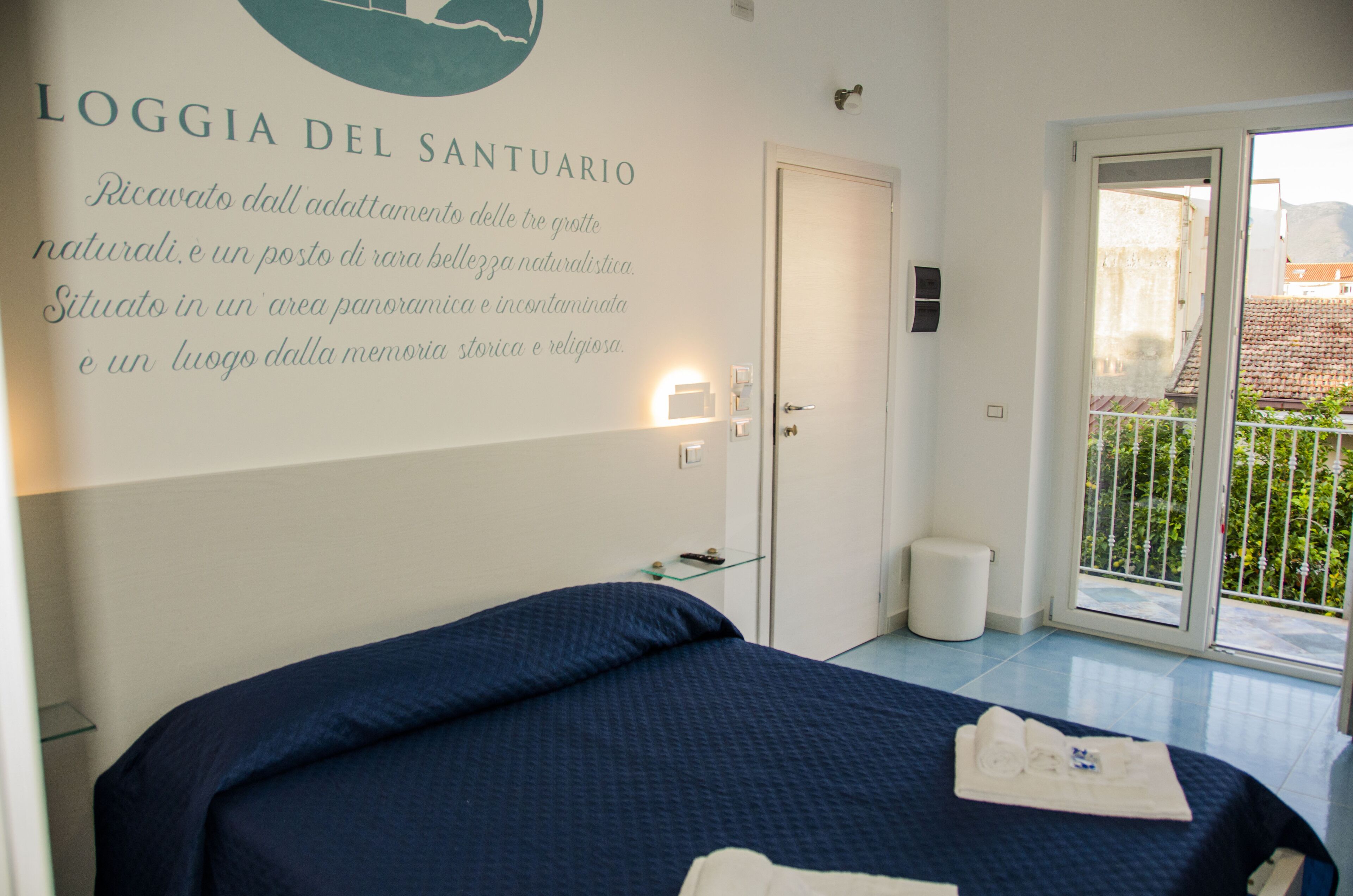 A hotel room with a bed, a glass door leading to a balcony, and a wall with text describing the location.