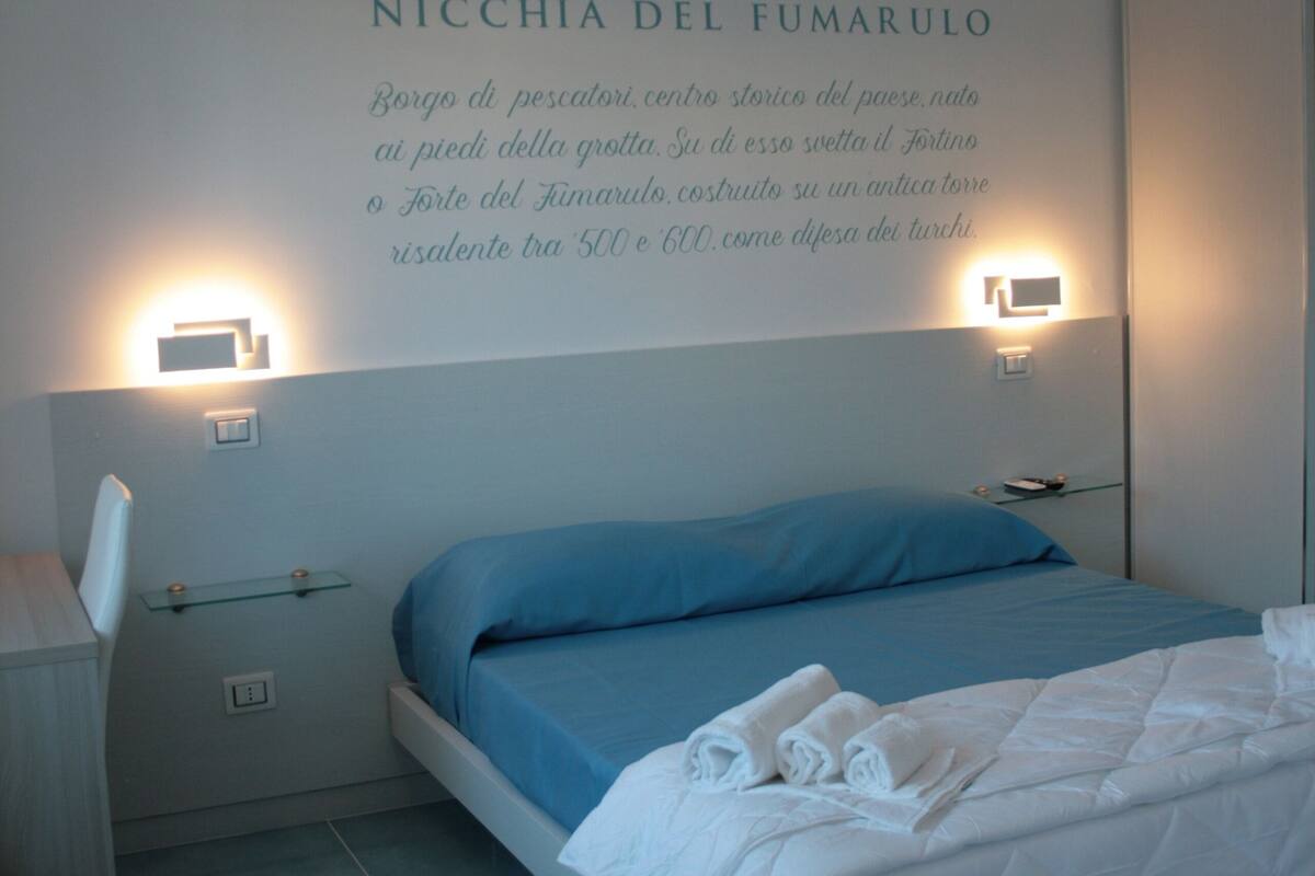 A hotel room with a bed, bedside tables, and a wall with a logo and text.