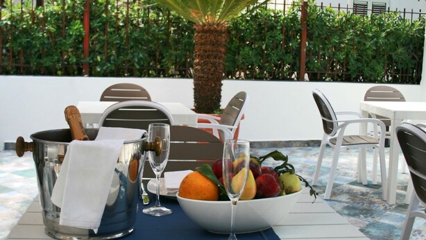 A table set for dining outdoors with a fruit bowl, wine glass, and a bottle of champagne. - Praja Vecchia (Praia a Mare)