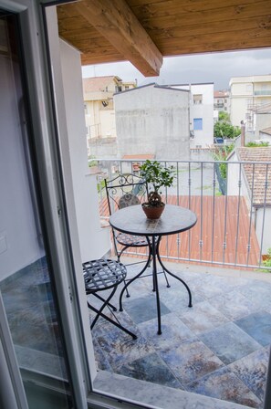 Un balcón con una mesa redonda y sillas, una planta en maceta y vistas a edificios cercanos.