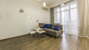 Ein modernes Wohnzimmer mit einem grauen Sofa, zwei weißen Beistelltischen und einer blauen Decke.