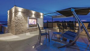 Une terrasse sur le toit, avec un mur en pierre, un écran de télévision et des sièges d’extérieur.