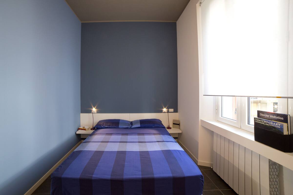 Una camera da letto con un letto, comodini, una finestra vista e un cartello appeso al vetro.