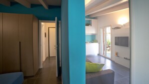 Un interno moderno con un corridoio che conduce a una cucina e a una zona living, caratterizzato da una parete azzurra, un divano e un televisore a schermo piatto.