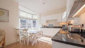 A modern kitchen with white cabinets, a black countertop, and a dining area with a table and chairs. - Carlton Lodge | Classic Seaside Charm | Parking (Broadstairs)