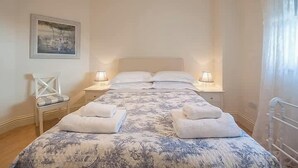 A bedroom with a bed, two bedside tables, a chair, and a painting on the wall. - Carlton Lodge | Classic Seaside Charm | Parking (Broadstairs)