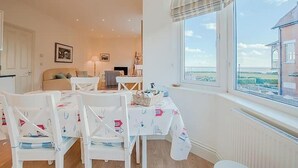 A dining area with white chairs and a table, a bed in the background, and a window with a view. - Carlton Lodge | Classic Seaside Charm | Parking (Broadstairs)